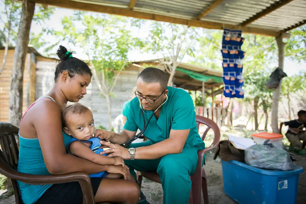 In a makeshift MTW health clinic in Honduras a local doctor examines a young boy held by his older sister